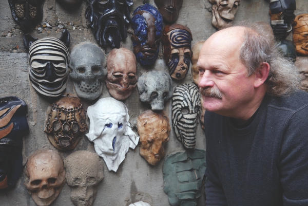 Portret Zbigniewa Mury na tle ściany z maskami ceramicznymi