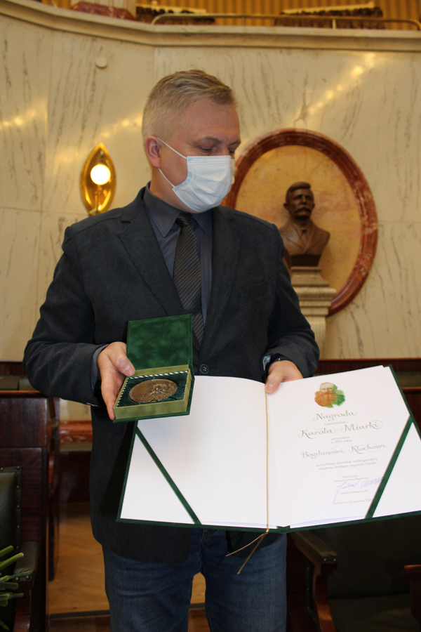 Mężczyzna - dr Bogdan Kloch pokazuje dyplom i medal nagrody im.  K.Miarki
