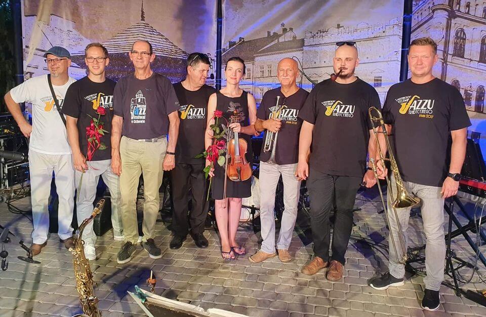 grupa 8 muzyków, stoją na scenie trzymając instrumenty